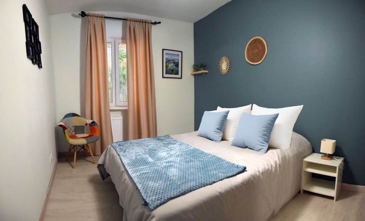 A bedroom with a bed, a chair, a nightstand, and a window with curtains.