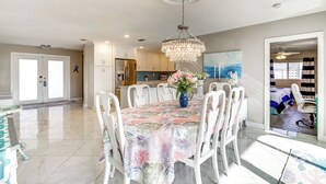 A spacious dining area with a chandelier, a table with a floral tablecloth, and a view of the kitchen in the background. - Centrally Located Cocoa Beach Haven: Walk to Shore (Cocoa Beach)
