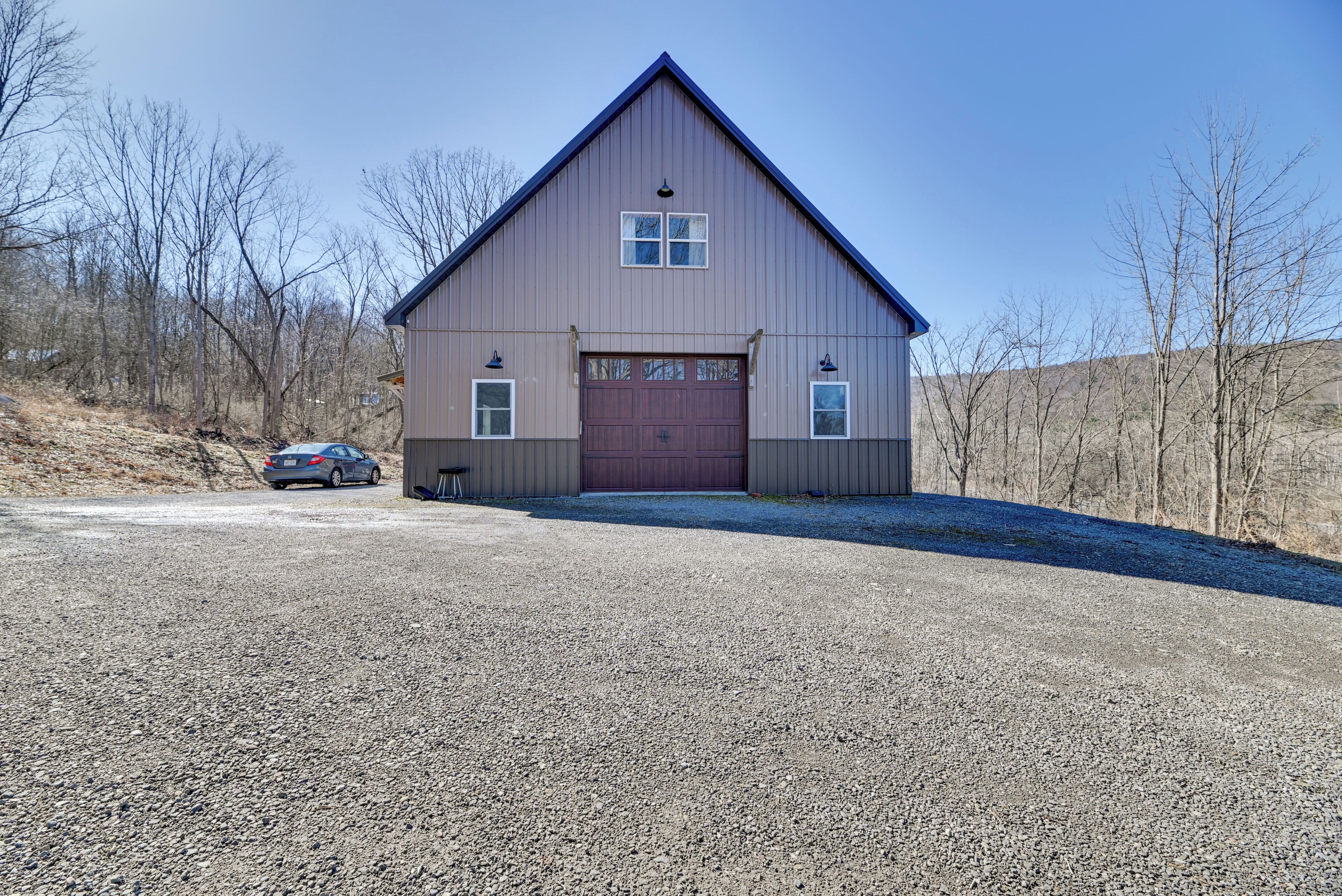 A single-story building with a red garage door, a small attached shed, and a gravel driveway.