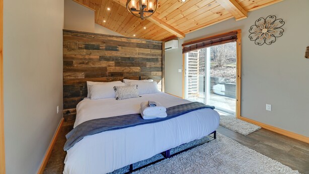 A bedroom with a wooden ceiling, a large bed with white bedding, and a view of the outdoors through a sliding door. - The Toasted Marshmallow Ski & Lake Game Barn (Canandaigua)