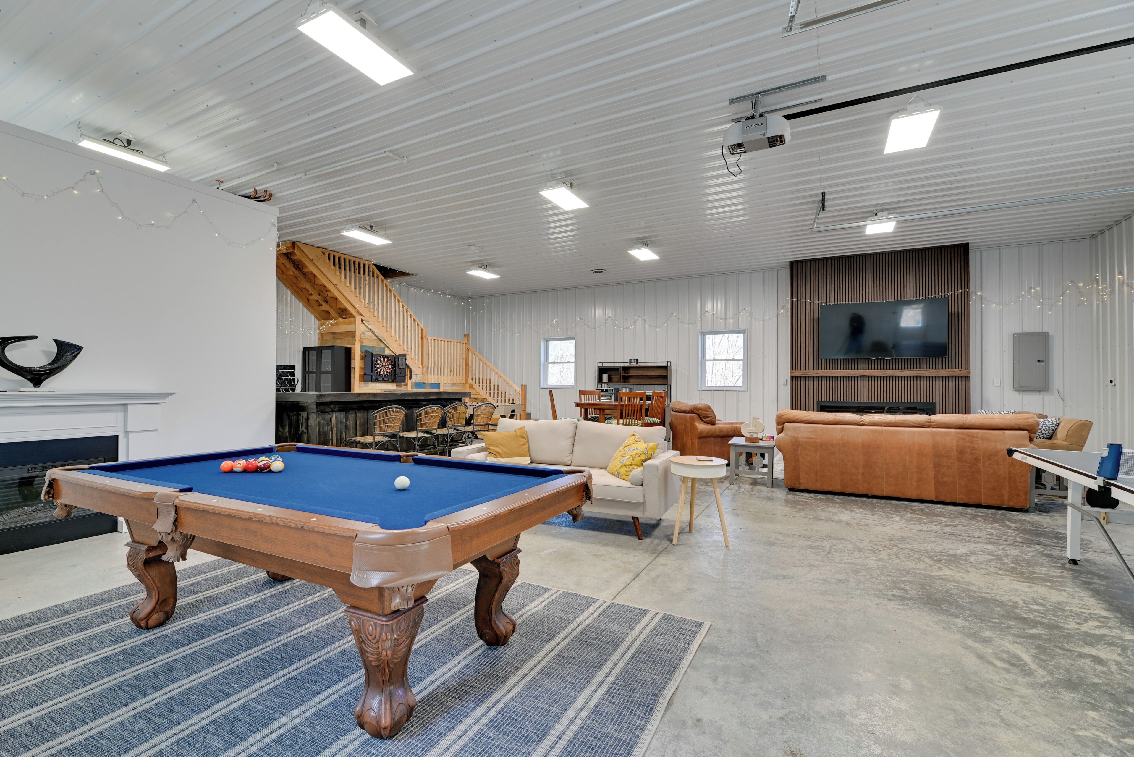 A spacious living area with a pool table, comfortable seating, a staircase, and a television.