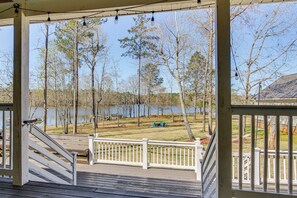 A wooden deck with a white railing, overlooking a grassy area with trees and a body of water. - Private Dock, Fire Pit: Lake Murray Family Escape! (Leesville)