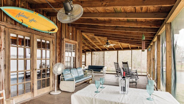 A wooden interior with a table set for dining, a surfboard, and seating areas. - Private Dock + Porch: Serene Lake Greenwood Escape (Greenwood)