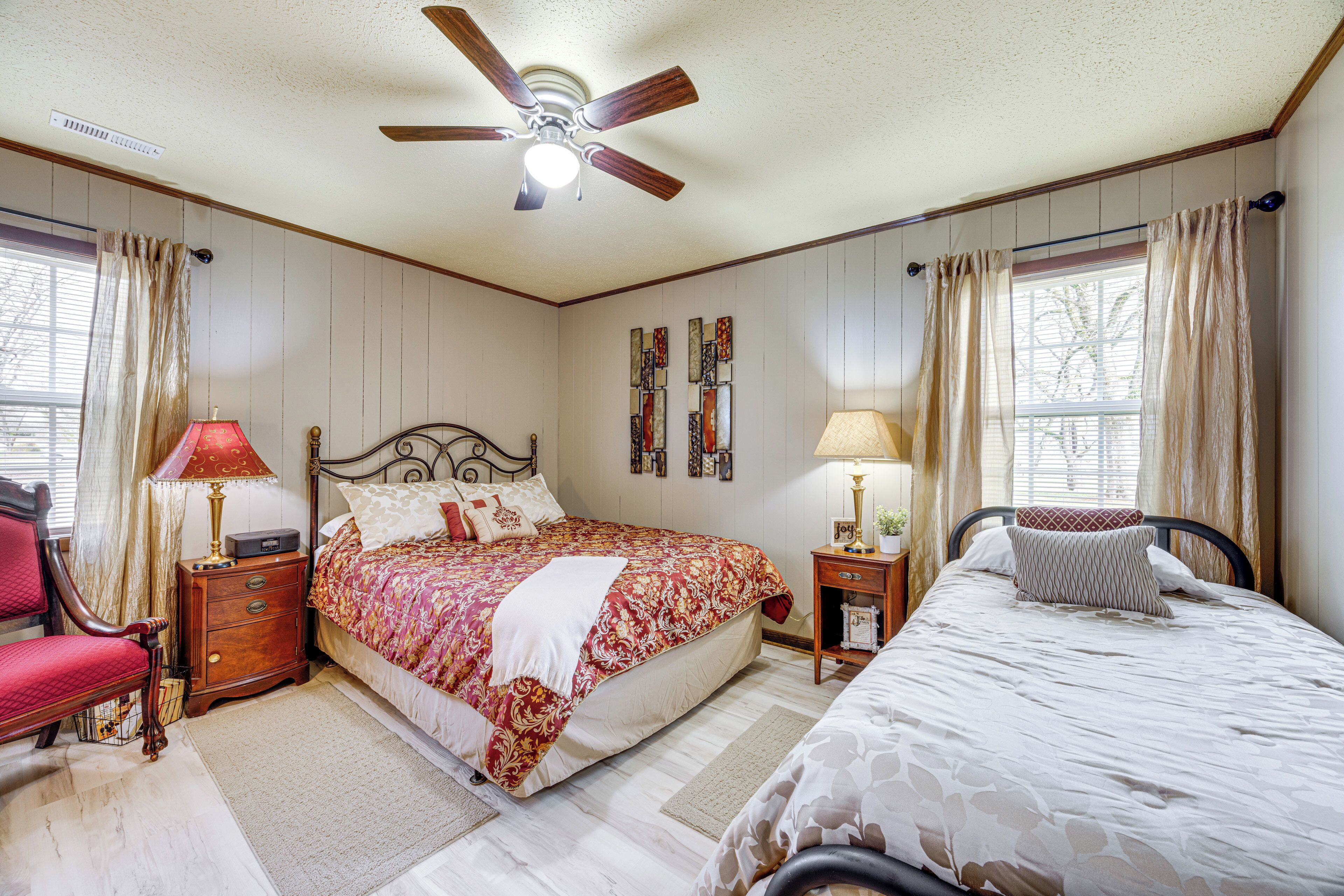A bedroom with a large bed, two bedside tables, a chair, a ceiling fan, and a window with curtains.