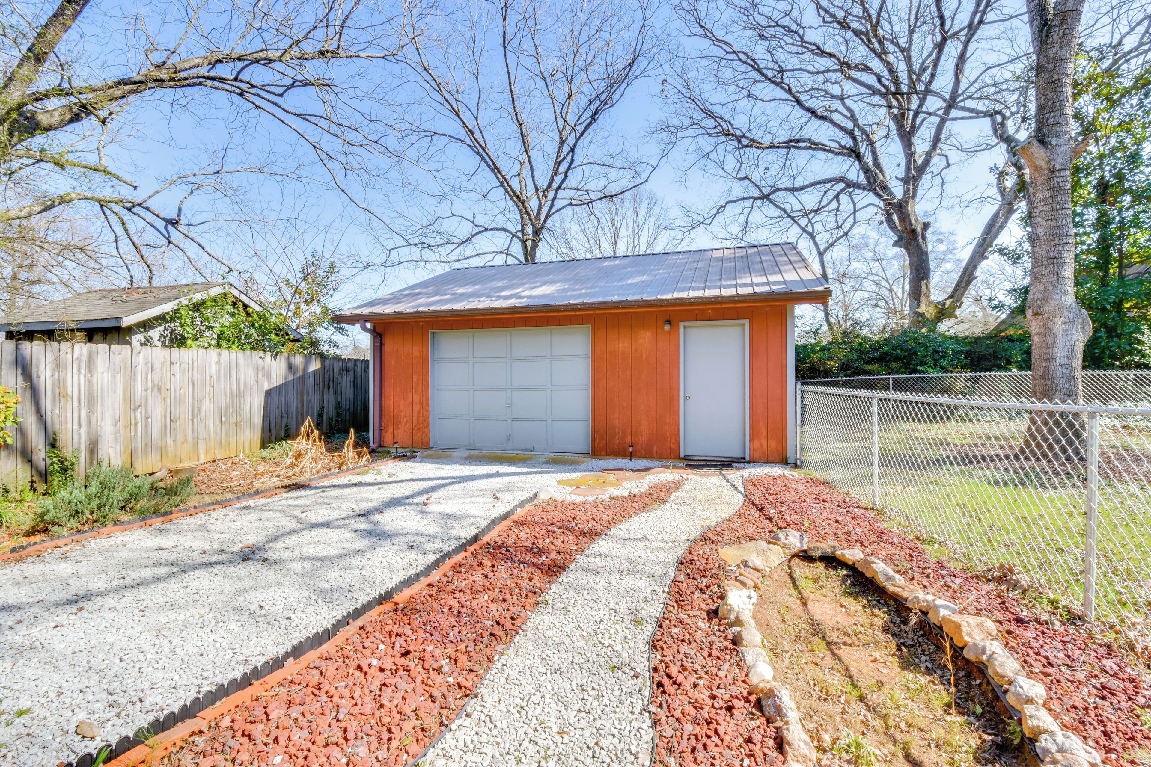 A garage with a metal roof, a wooden door, and a gravel driveway with red and white stones.