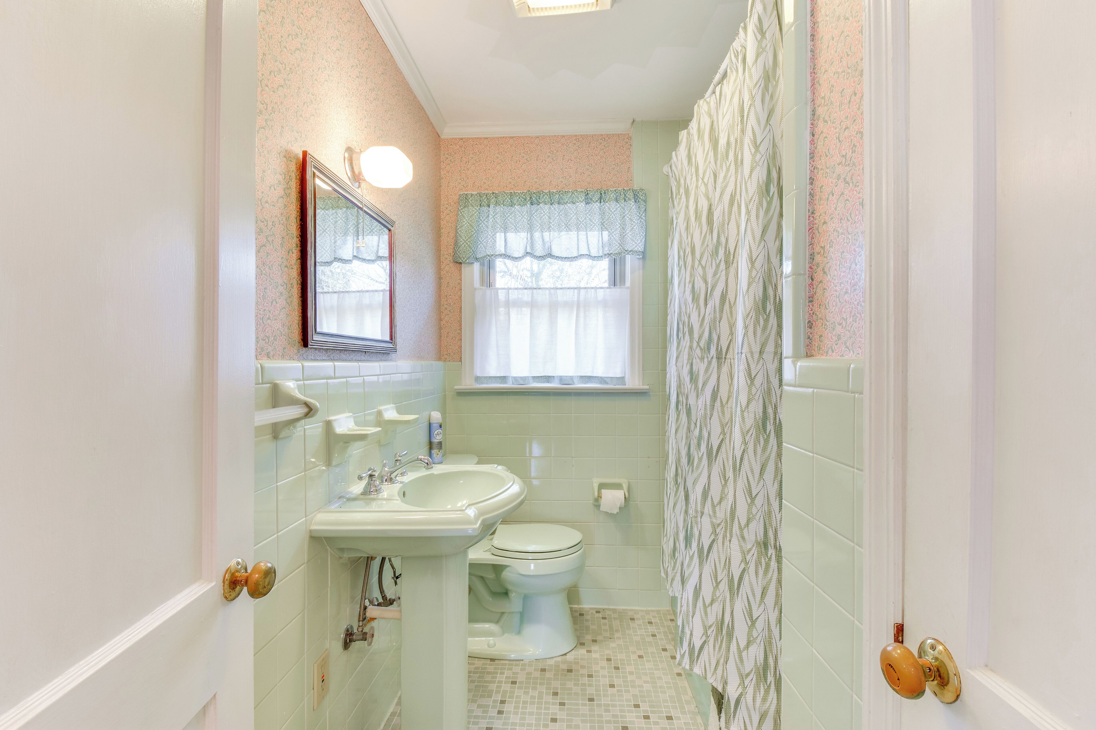 A bathroom with a sink, toilet, and window with a patterned curtain.