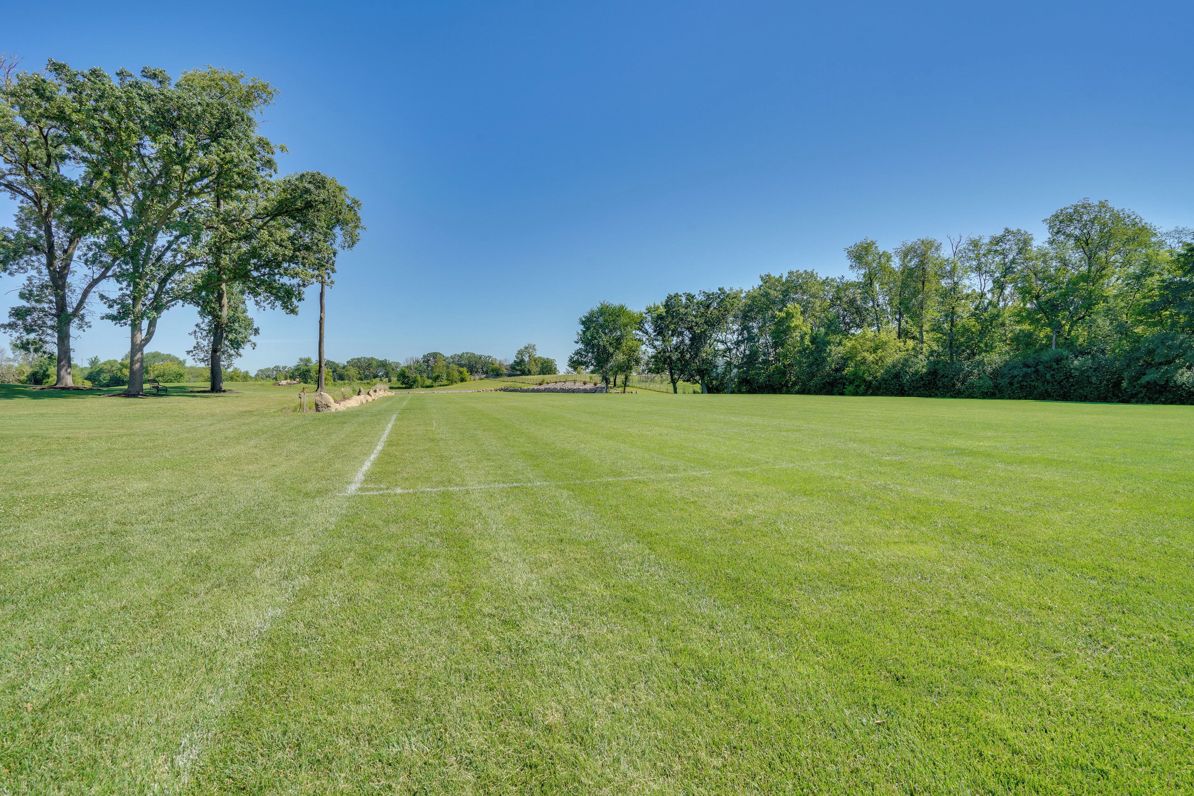 A well-maintained grassy field with trees and a clear blue sky.