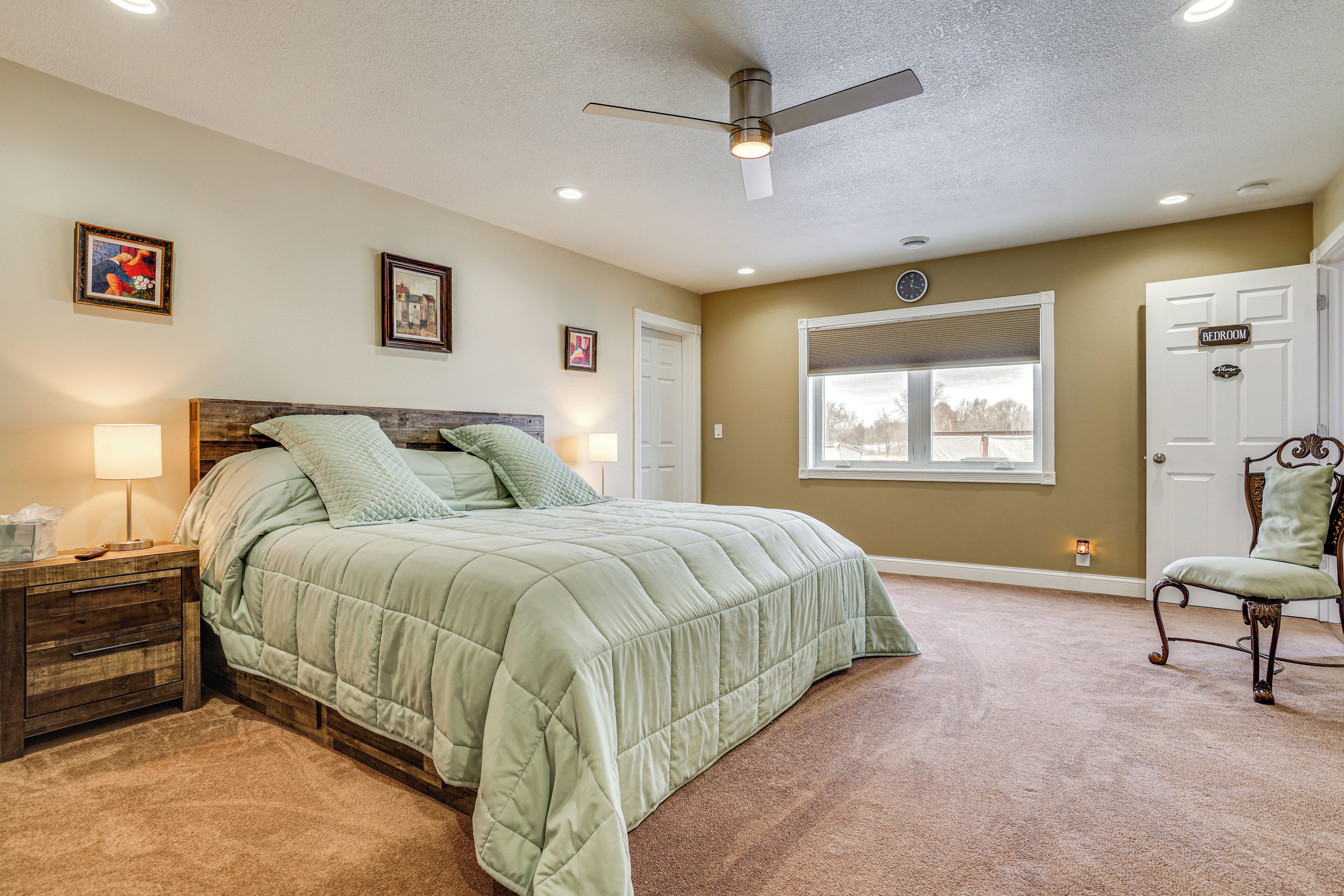 A bedroom with a bed, nightstands, a chair, a ceiling fan, and a window.