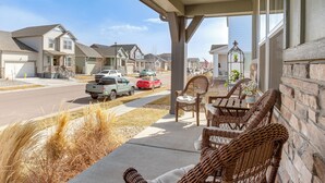 A covered porch with wicker furniture, a street view, and residential houses in the background. - Beautiful Home w/ Bonus Room & Prime Location! (Brighton)
