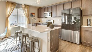 A modern kitchen with stainless steel appliances, a large island with bar stools, and wooden cabinetry. - Beautiful Home w/ Bonus Room & Prime Location! (Brighton)