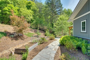A stone pathway leading to a house with a wooden deck and a garden with various plants and trees.