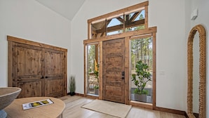 Une porte en bois avec un panneau de verre, un paillasson en fibres naturelles à l’entrée et une tapisserie murale tissée.