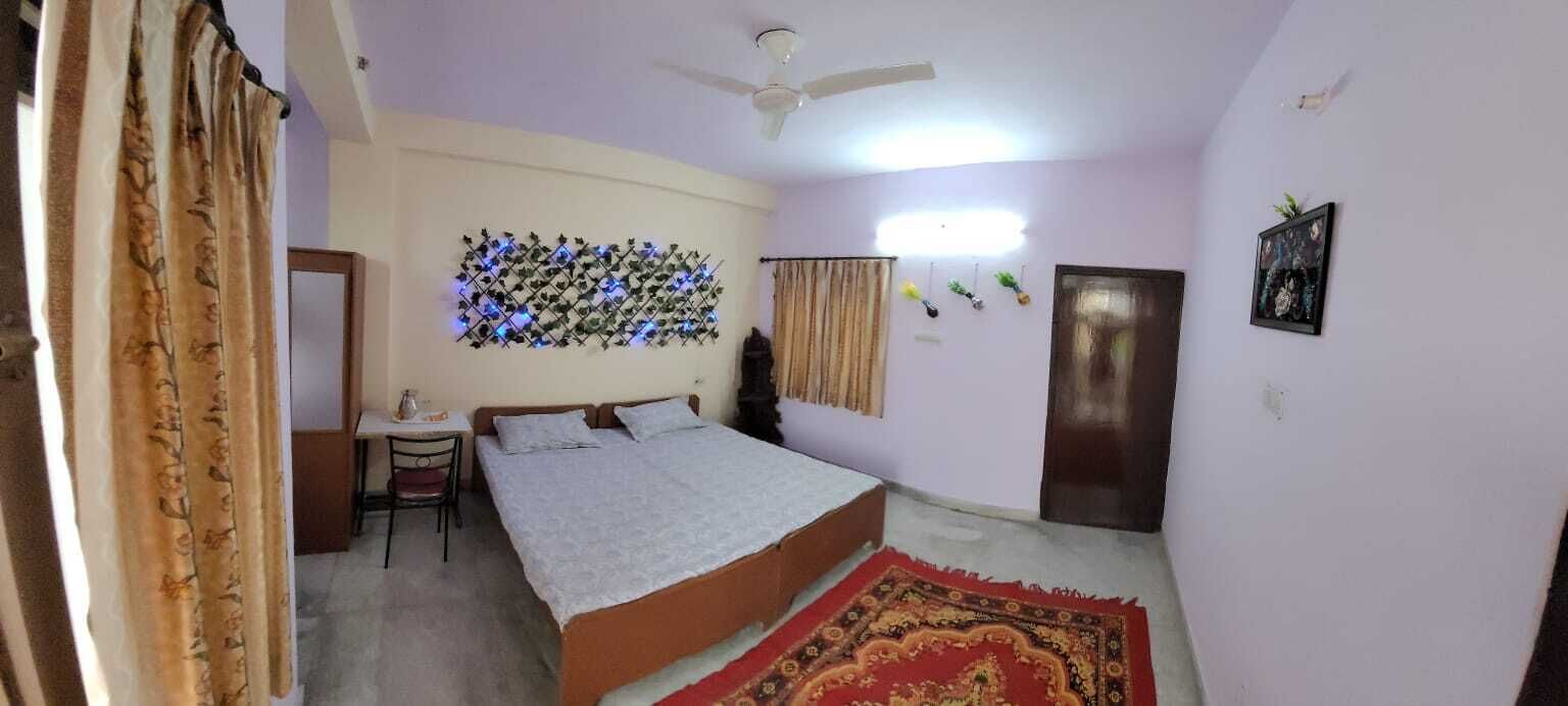 A bedroom with a bed, a desk, a chair, a ceiling fan, a wall-mounted light, a door, and a wall decoration.