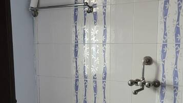 Zona de ducha con pared de azulejos, ducha, alcachofa de ducha manual y un cubo rosa en el suelo.