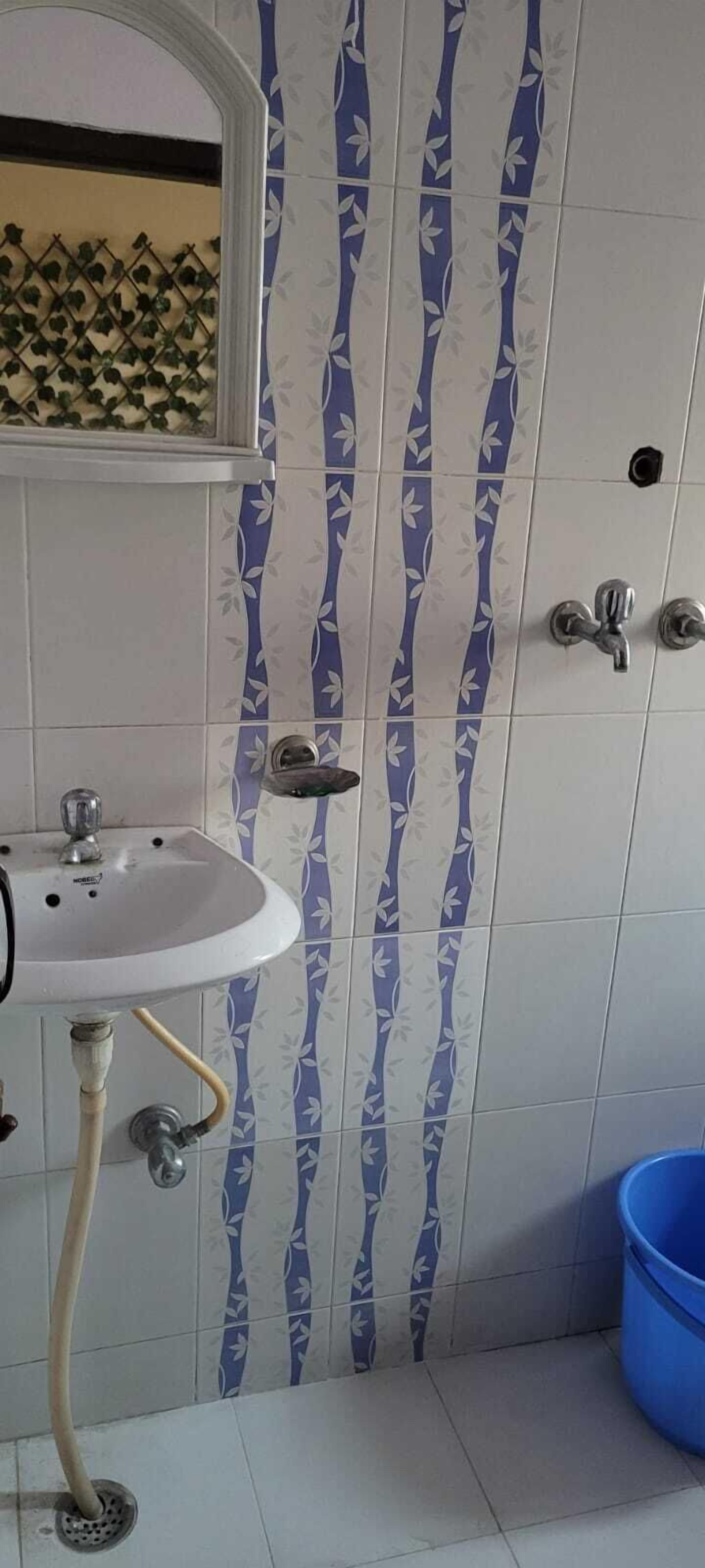 Uma casa de banho com uma pia, chuveiro e um balde azul.