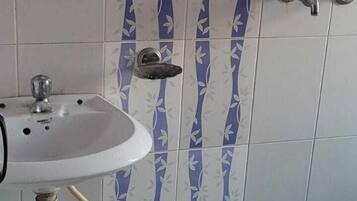 Uma casa de banho com uma pia, chuveiro e um balde azul.