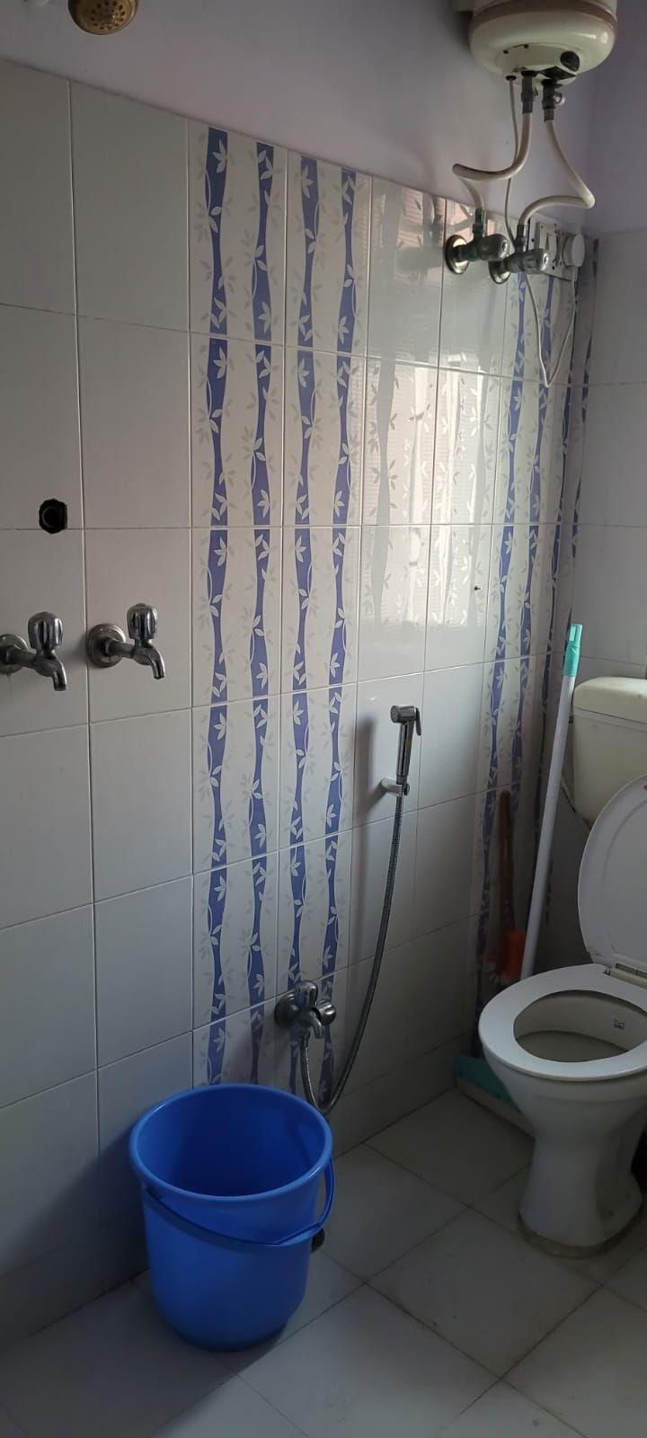 Casa de banho com sanita, chuveiro e um balde azul.