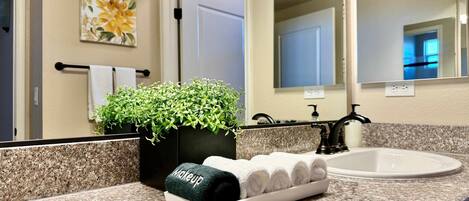 Un baño con encimera de granito, un lavabo, un espejo, una planta en maceta y un perchero con una toalla blanca.