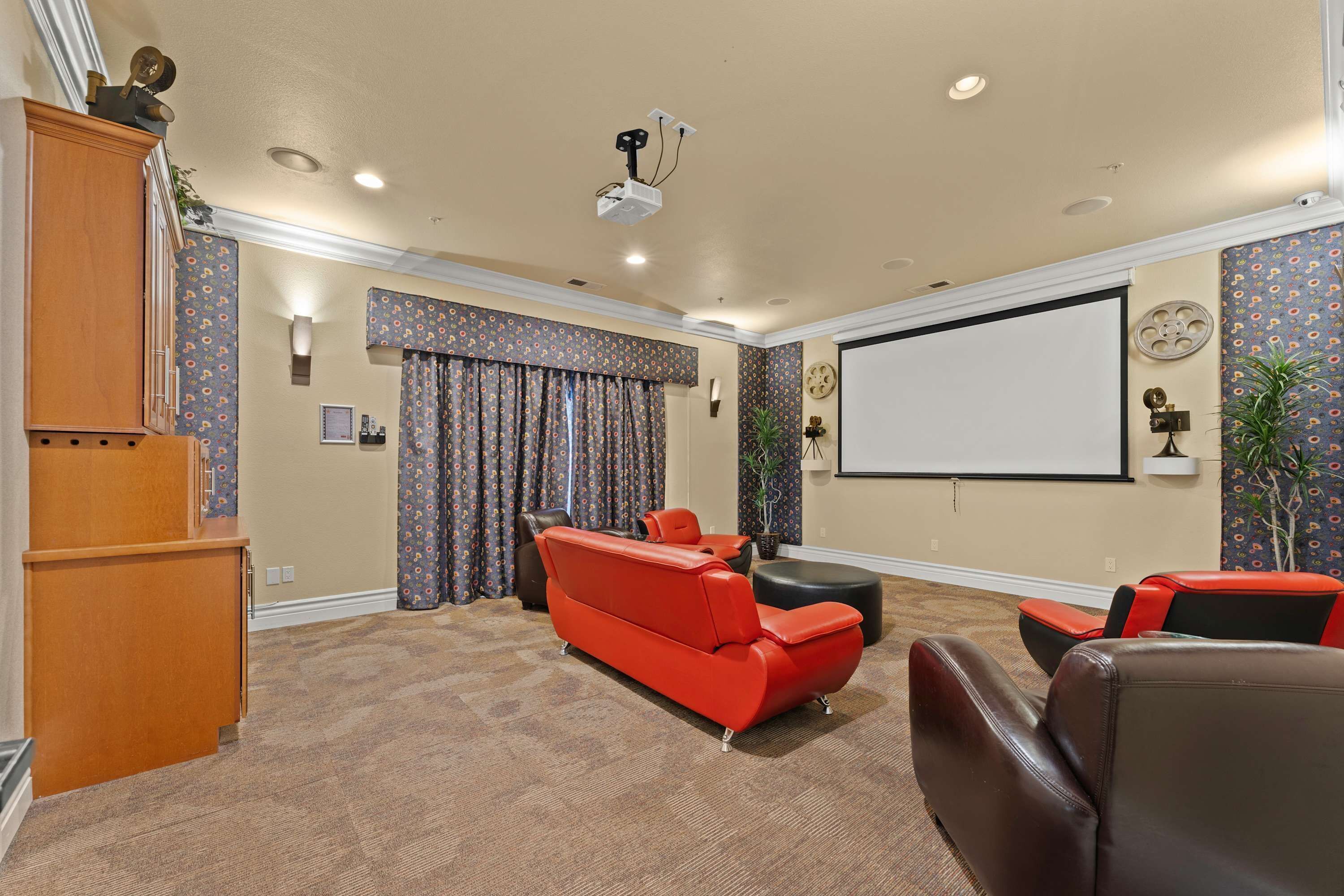 A home theater room with a large screen, red and black leather seating, carpeted floor, and patterned wallpaper.