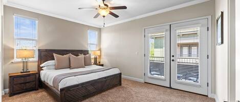 A bedroom with a bed, two bedside tables, a ceiling fan, and a door with a balcony.