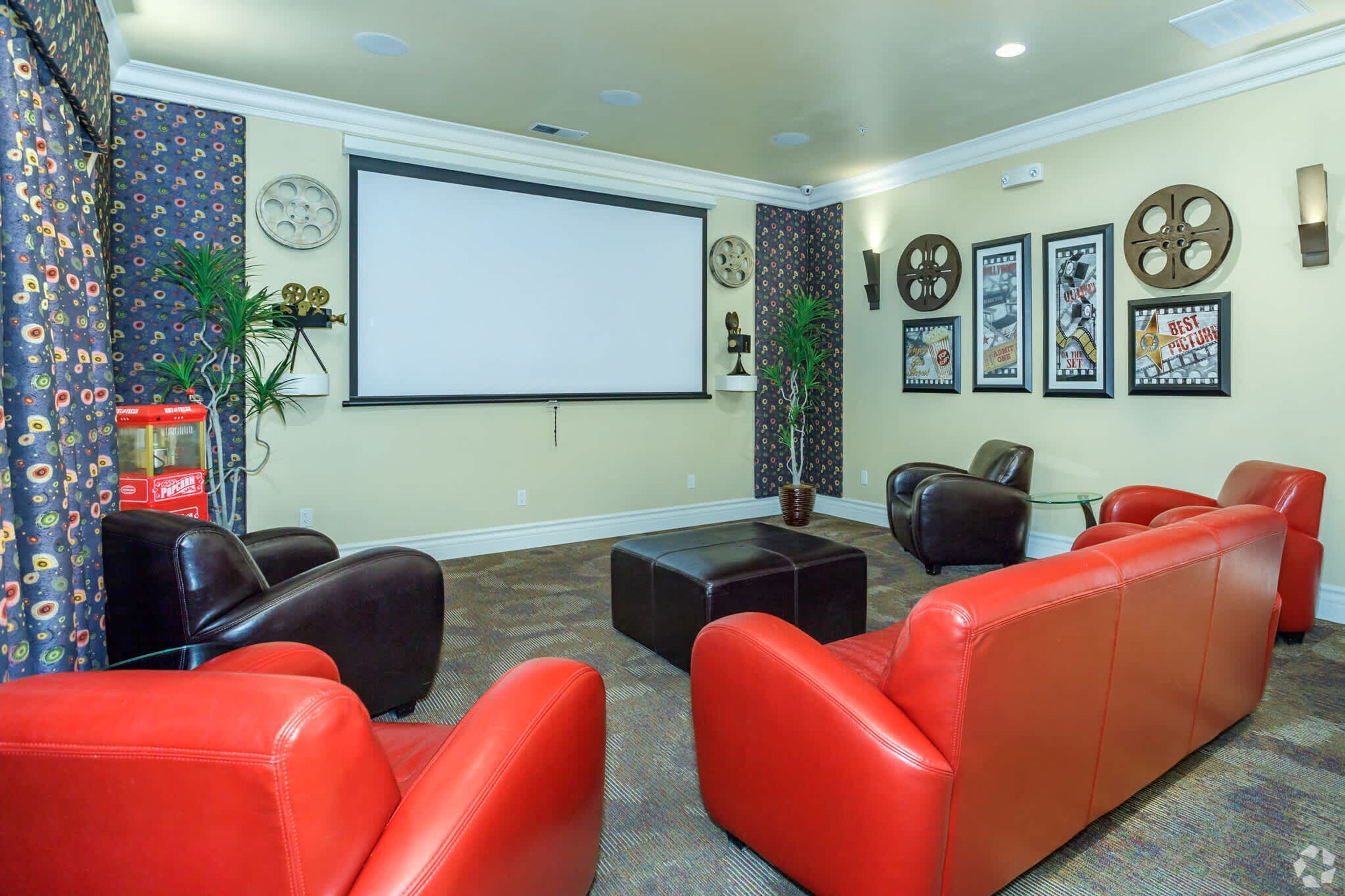 Un espace détente avec des canapés en cuir rouge et noir, un grand écran et des affiches de films accrochées au mur.
