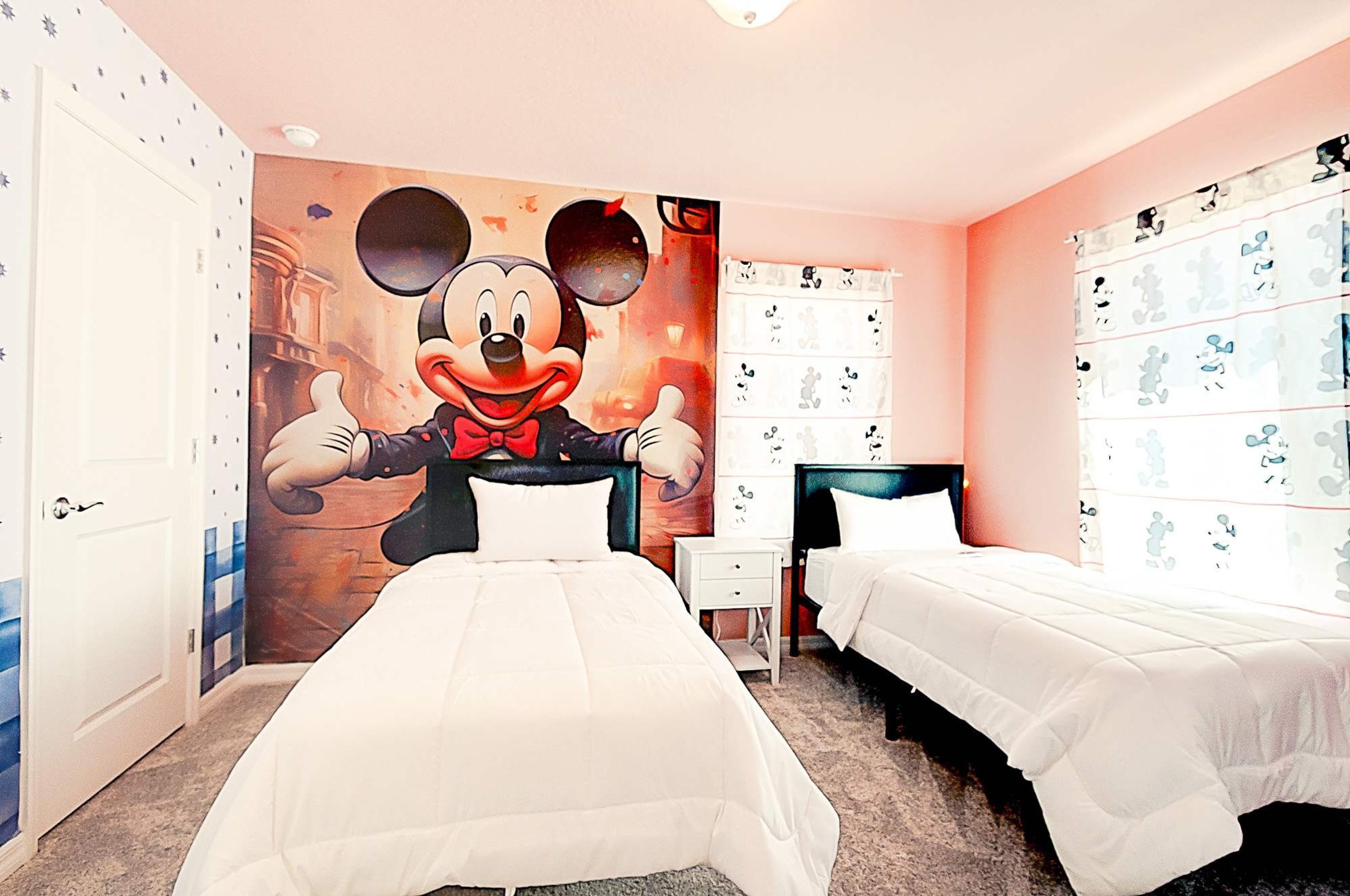 Camera d'albergo con due letti, un grande murale di Topolino sulla parete e arredamento a tema Topolino.