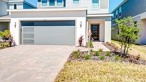 A modern two-story house with a garage, a well-maintained lawn, and a small tree in the front yard. - 15976 Spacious Charming Family Getaway (Clermont)