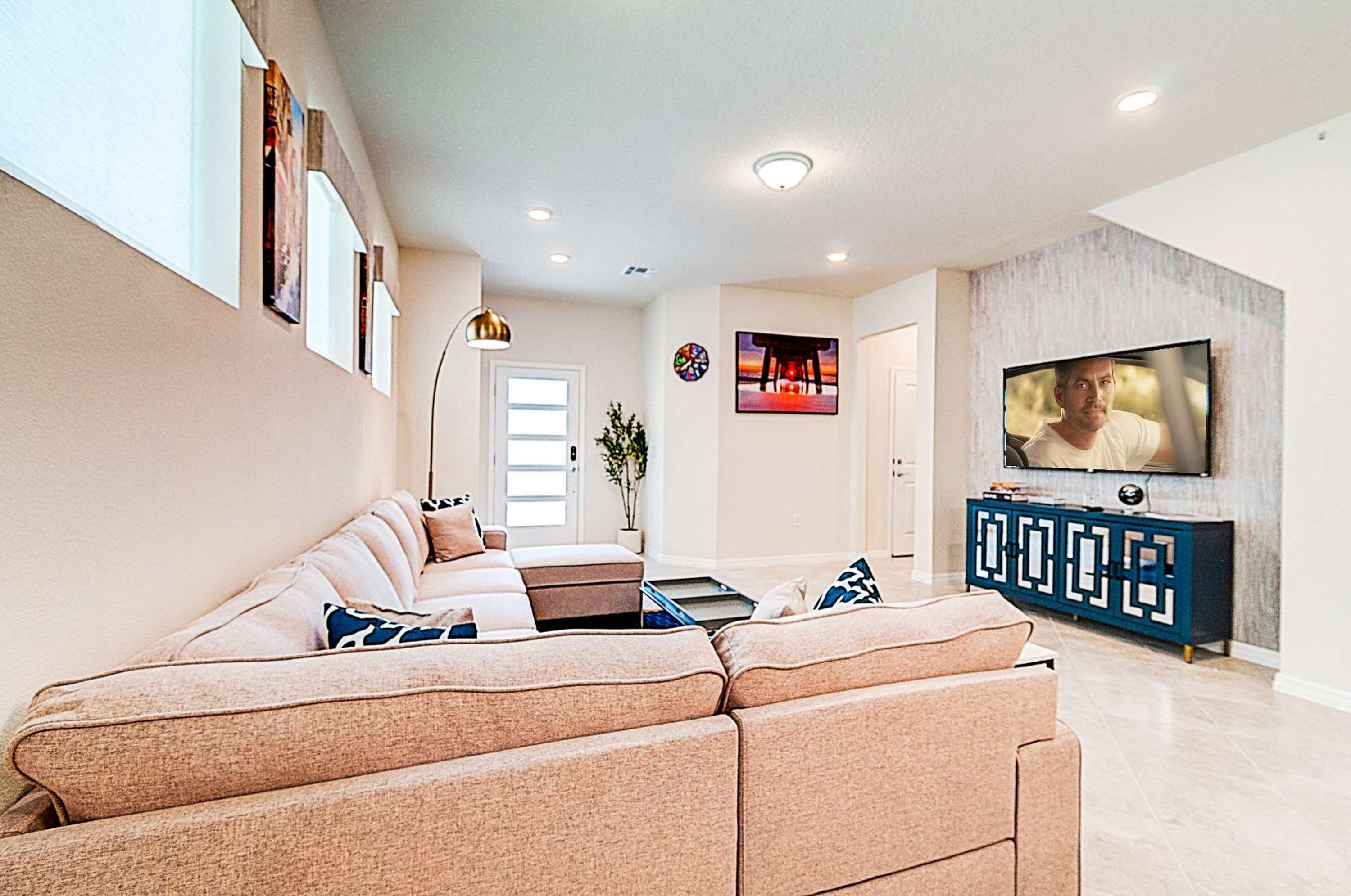 Una sala de estar moderna con un sofá seccional color beige, un televisor de pantalla plana montado en la pared y un mueble azul con diseños geométricos.