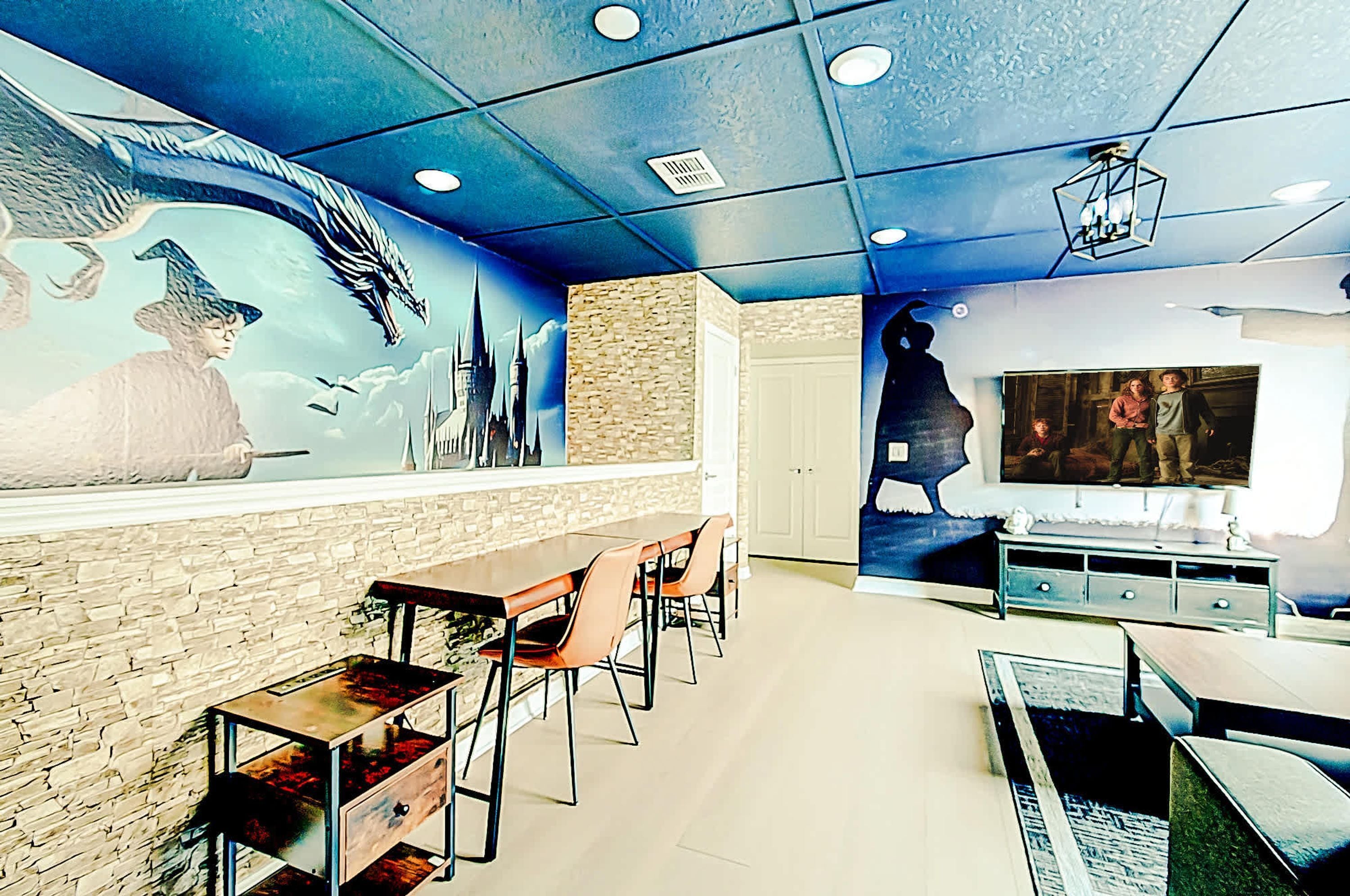 Een restaurant met een muurschildering van een draak en een tovenaar, een stenen muur en een televisiescherm.