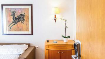 Una habitación de hotel con una cama, un armario de madera, una lámpara de pared y una obra de arte enmarcada.