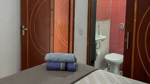 A room with a bed, a wooden door, and a bathroom visible through an open door.