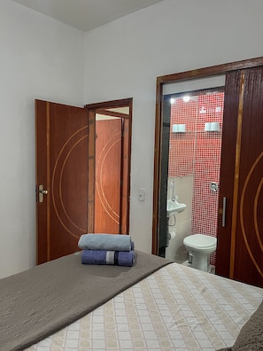 A room with a bed, a wooden door, and a bathroom visible through an open door.