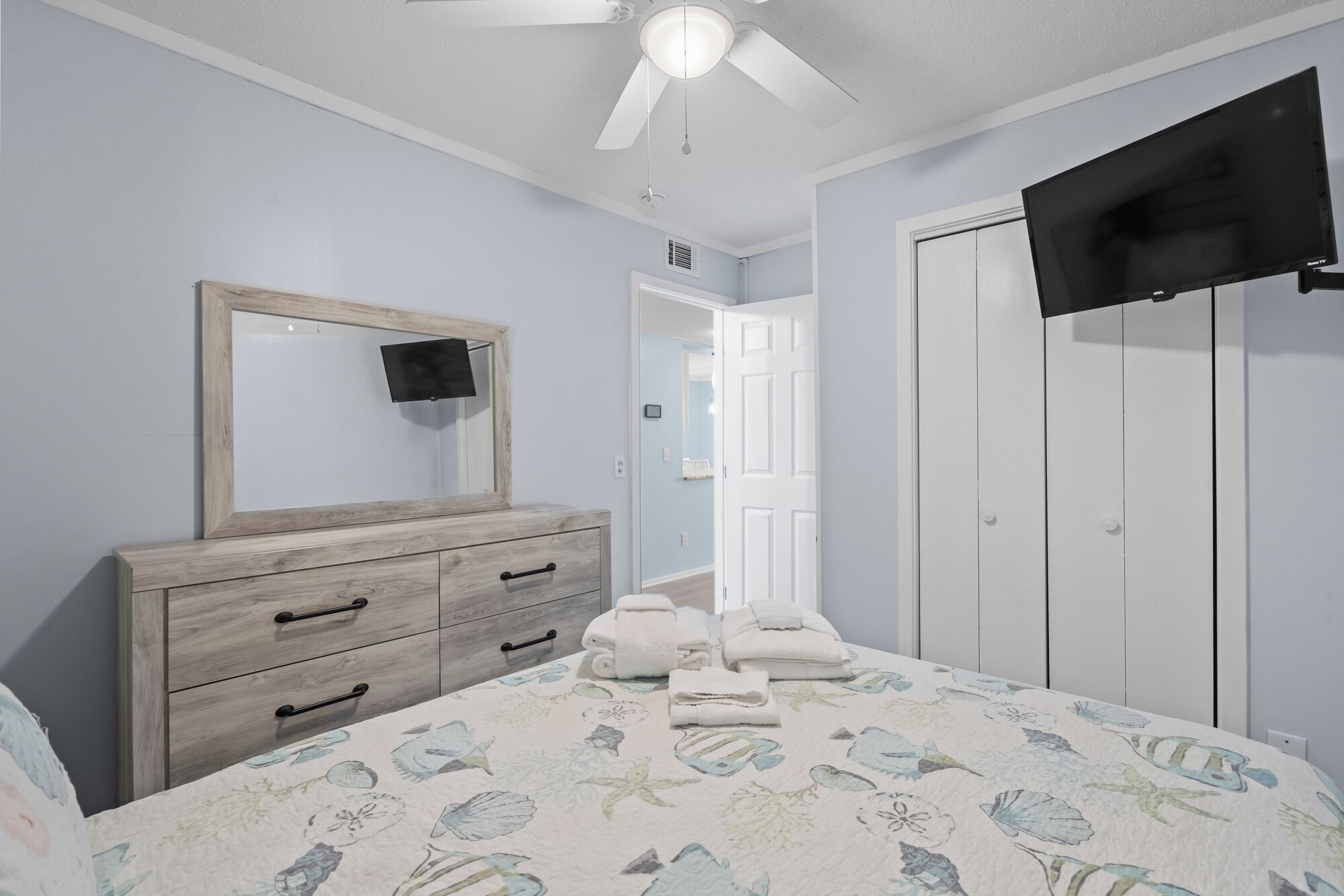 A bedroom with a bed, dresser, TV, and a door leading to another room.