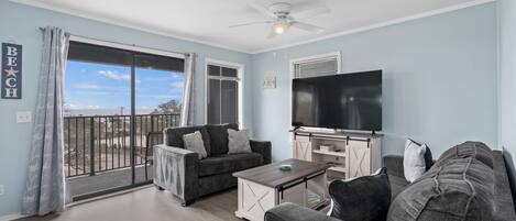 A living room with a balcony, a ceiling fan, a flat-screen TV, and a sofa.