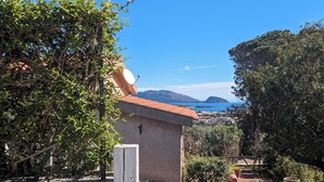 A stone sign with "Stella Marina" written on it, a building with a red roof, and a view of the sea and mountains in the background.