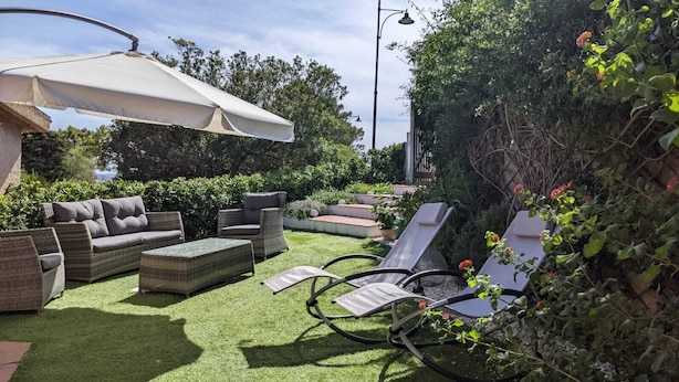 An outdoor patio with wicker furniture, a white umbrella, and a well-maintained garden.