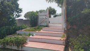 A set of outdoor steps leading to a gated entrance, surrounded by greenery and a street lamp.