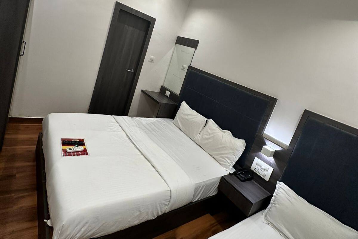 A modern hotel room with a large bed, a smaller bed, a bedside table with a lamp, a mirror, and an air conditioning unit.