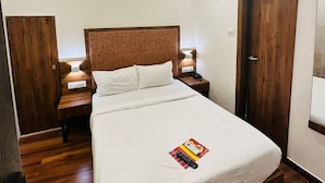 A hotel room with a single bed, wooden headboard, bedside tables with lamps, an air conditioning unit, and a ceiling fan.
