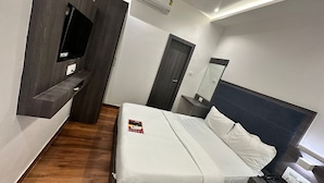 A modern hotel room with a bed, a flat-screen TV mounted on a dark wall, an air conditioning unit, and a ceiling fan.