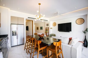 A modern kitchen with a dining area, a ceiling fan, and a flat-screen TV mounted on the wall.