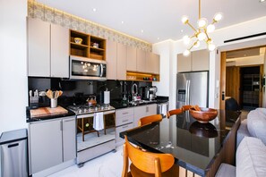 A modern kitchen with a central island, stainless steel appliances, and a dining area with a black table and wooden chairs.