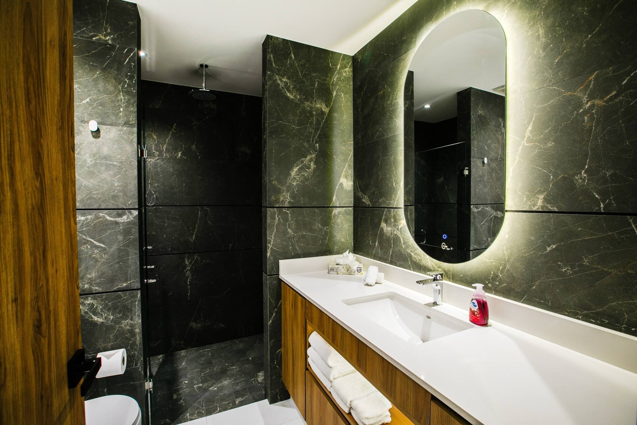 A modern bathroom with a large mirror, a shower, and a vanity with a sink and towel rack.