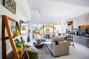 A modern living room with a sofa, coffee table, and a dining area with a kitchen in the background.