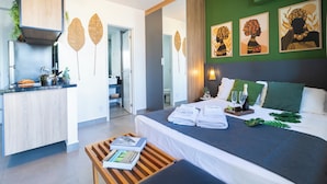Ein modernes Hotelzimmer mit Bett, einem Holztischchen, einer Küchenzeile und Kunstwerken an den Wänden.
