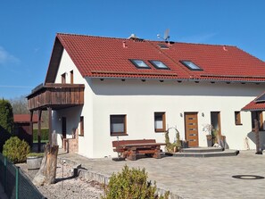 Kaksikerroksinen talo, jossa on punatiilinen katto, parveke ja puinen terassi.