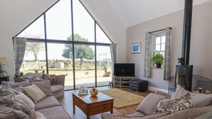 A spacious living room with a large window, a flat-screen TV, a fireplace, and a comfortable sofa set. - Crossett Grange (Driffield)