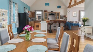 A spacious kitchen with wooden beams, a dining area with a wooden table and chairs, and a living area with a sofa and a coffee table. - Crossett Grange (Driffield)