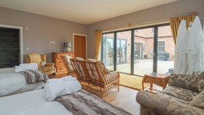 A spacious bedroom with a large bed, a sofa, and a chair. There is a sliding glass door leading to a patio with a brick wall and a garden. - Crossett Grange (Driffield)