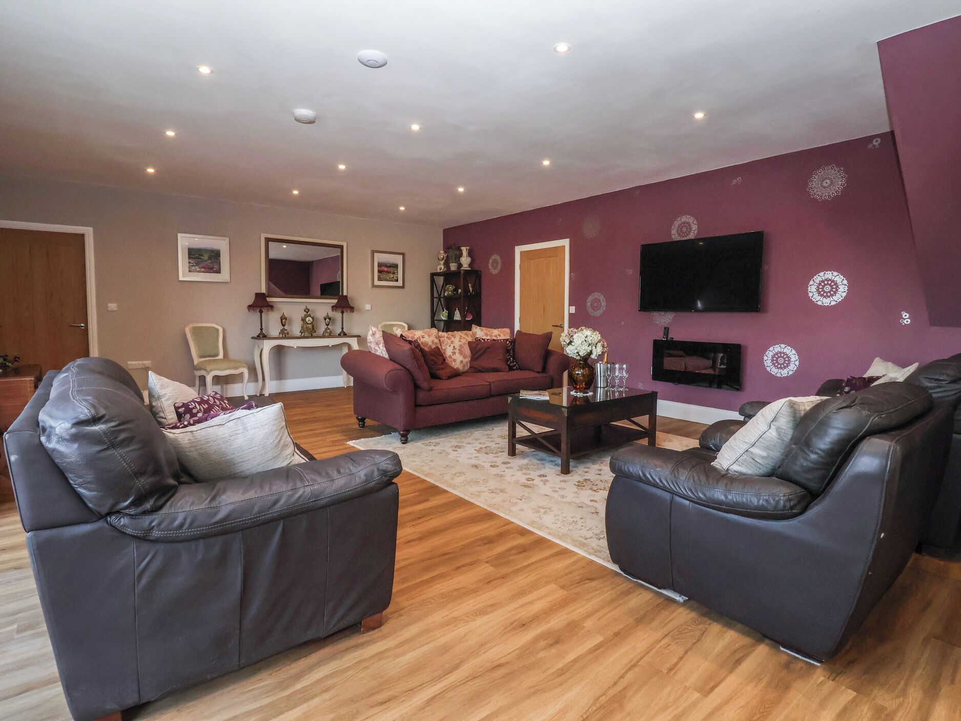 Un salon comprenant un canapé, deux fauteuils, une table basse et un téléviseur fixé au mur.